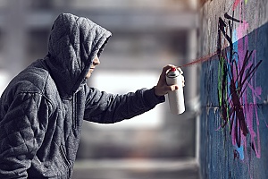 a criminal spraying graffiti on a wall in a public park