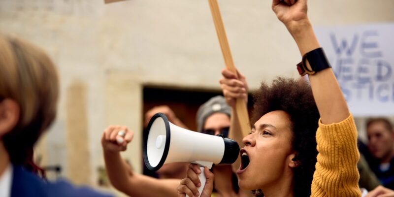 african american woman with raised fist shouting through megaphone