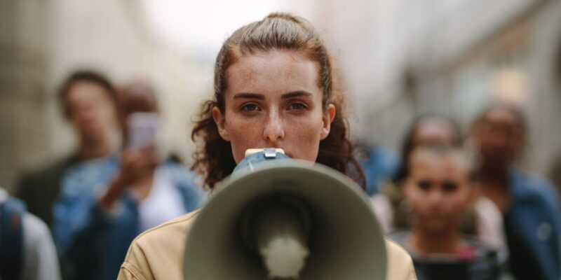 female activist protesting with megaphone during a strike with group of demonstrator in background