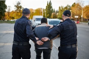 Two police officers arresting a man and taking him to the car