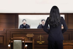 A female attorney is representing a case before two judges in the courtroom