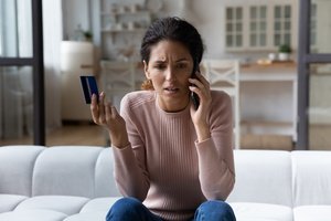 A frustrated woman is talking with someone on a call while holding a credit card