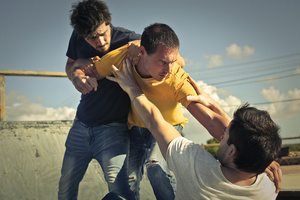 Two young men fighting while one is trying to resolve